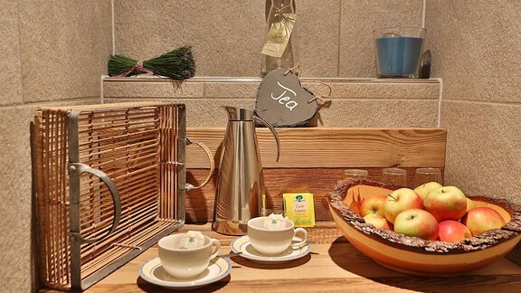 A cozy tea table with two cups, a pot, and a bowl full of fresh apples. In the background, some herbs hang and a sign reads "Tea." - Haus Söldenblick - Sölden