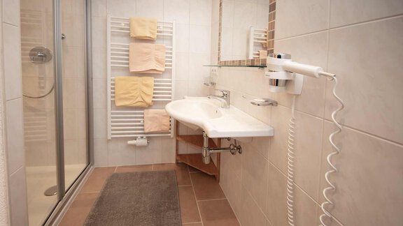 A modern bathroom with a shower and a sink. Towels are placed on a towel rack, and the floor is covered with a rug. - Haus Sonnwend - Sölden