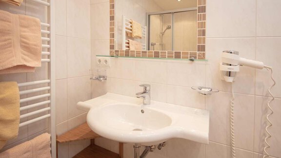 A modern bathroom with a white sink and a large mirror. Towels and a hairdryer are also visible. - Haus Sonnwend - Sölden