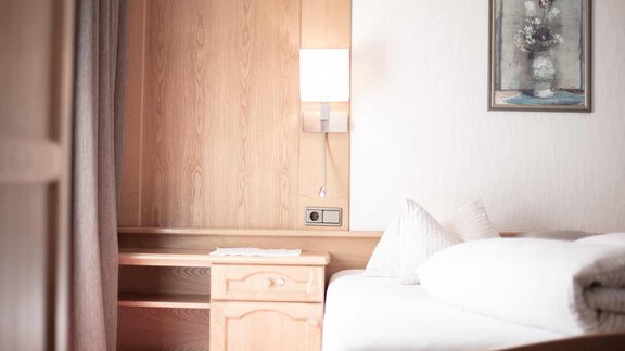 A cozy bedroom with a wooden wardrobe and a bedside table. A painting of a floral still life hangs on the wall. - Haus Sonnwend - Sölden