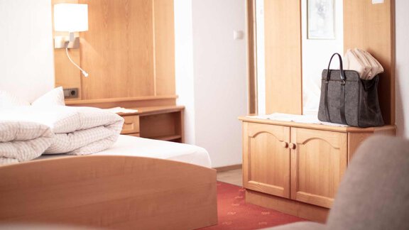 A cozy room with a bed, fresh bed linens, and a wardrobe. A bag is on a sideboard in the corner. - Haus Sonnwend - Sölden
