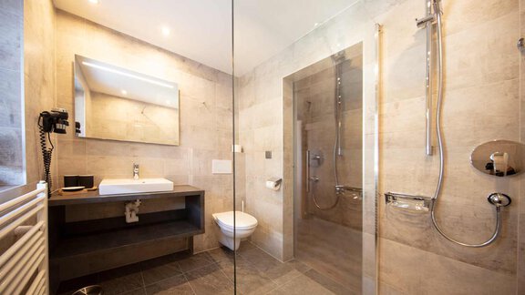 A modern bathroom with a glass shower enclosure. There is a sink and an elegant mirror on the wall. - Haus Sonnwend - Sölden