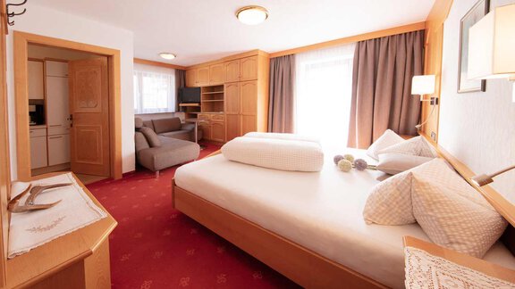 A cozy hotel room with a large bed and a living area. Bright colors and wooden details give the space a warm atmosphere. - Haus Sonnwend - Sölden