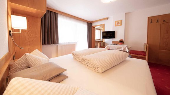 A cozy hotel room with a large bed and beige pillows. There is a television and a small table in a bright, inviting space. - Haus Sonnwend - Sölden