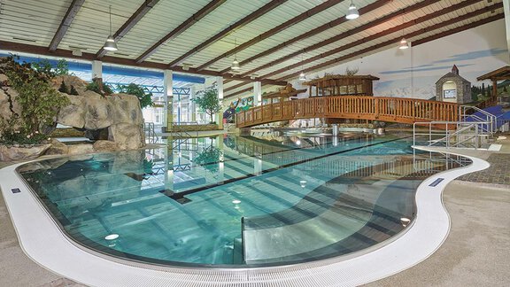 An indoor pool with clear water and a curved shape. The area is surrounded by wooden bridges and plants. - Haus Sonnwend - Sölden