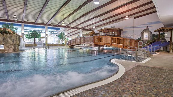 An indoor pool with a wooden bridge and a slide. Surrounded by plants and good lighting, it creates a relaxing atmosphere. - Haus Sonnwend - Sölden