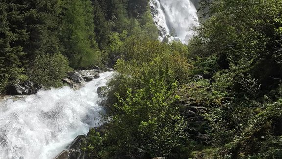 An impressive waterfall flows through a green landscape. Tall trees and mountains surround the scene under a blue sky. - Haus Sonnwend - Sölden
