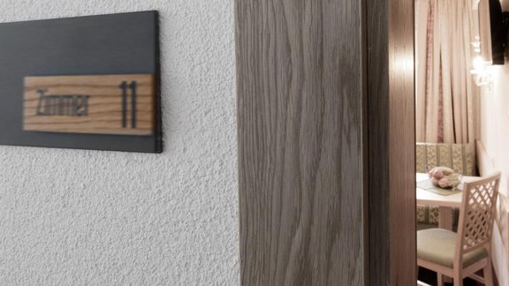 A view of the door to room 11, with a wooden plaque displaying the room name. In the background, a part of the room with a table and chairs is visible. - Haus Stefanie - Sölden
