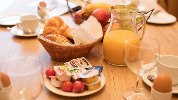 A breakfast table with a bowl of fresh fruit, croissants, and yogurt. There's also orange juice and coffee. - Haus Stefanie - Sölden