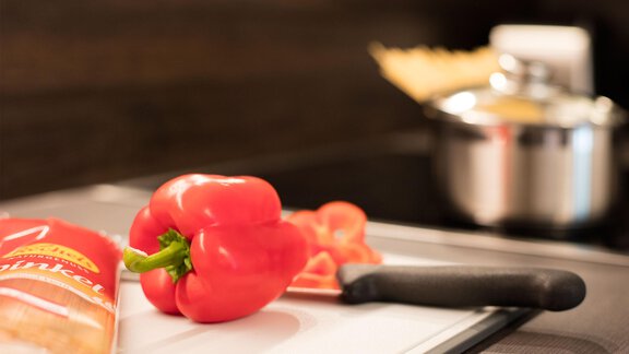 A red bell pepper lies on a cutting board next to a knife. In the background, there's a pot and a rolling pin. - Haus Stefanie - Sölden