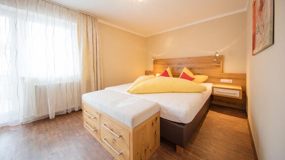 A bright bedroom with a large bed and cozy pillows. White curtains let in plenty of light and create an inviting atmosphere. - Haus Stefanie - Sölden