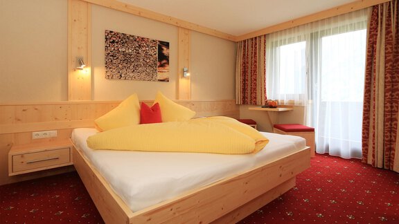 A cozy bedroom with a large bed and colorful pillows. Bright walls and a window with curtains create an inviting atmosphere. - Haus Stefanie - Sölden