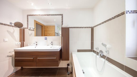 A modern bathroom with a large sink and a bathtub. The walls are in neutral colors and there are wooden details. - Haus Stefanie - Sölden