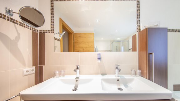 A modern bathroom with a large double sink and a mirror. The walls are painted in neutral colors, and there are wooden accents. - Haus Stefanie - Sölden