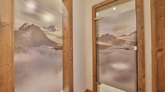 Two glass doors with mountain motifs that transition into a foggy background. The frame is made of wood and conveys a warm atmosphere. - Haus Söldenblick - Sölden