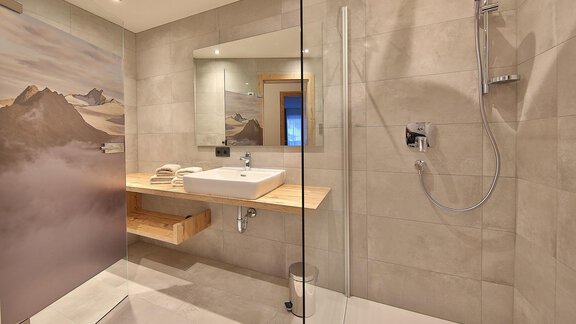 A modern bathroom with a transparent shower and a wooden countertop. The space has bright walls and an elegant, minimalist design. - Haus Söldenblick - Sölden