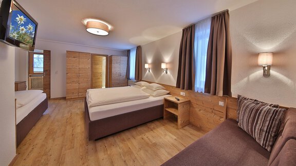 A modern hotel room with two beds, a couch, and a television. The walls are neutral, and the lighting is cozy. - Haus Söldenblick - Sölden
