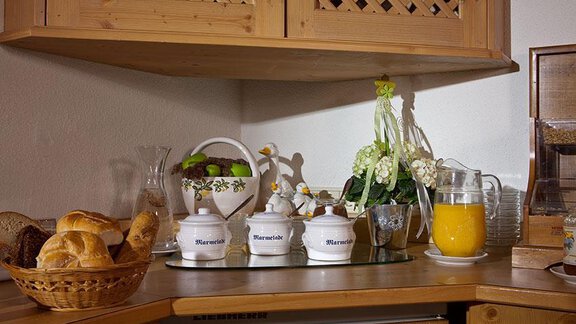A cozy kitchen corner with fresh rolls, orange juice, and a decorative teapot. Flowers and dishes give the scene an inviting touch. - Hotel Garni Ehrenreich - Sölden