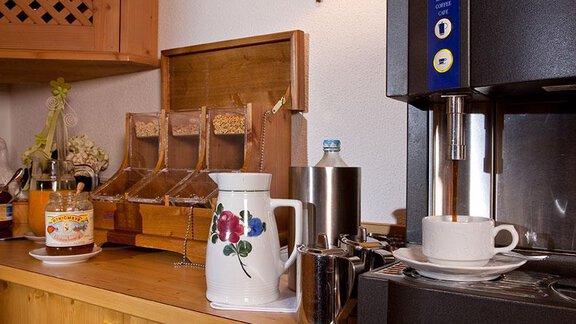 A cozy kitchen corner with a coffee machine and a stylish kettle. There are also some storage containers and a cup on the table. - Hotel Garni Ehrenreich - Sölden