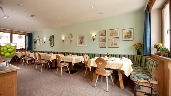 A friendly, bright restaurant space with set tables and cozy benches. Pictures hang on the walls, and decorative plants give the room an inviting atmosphere. - Hotel Garni Ehrenreich - Sölden