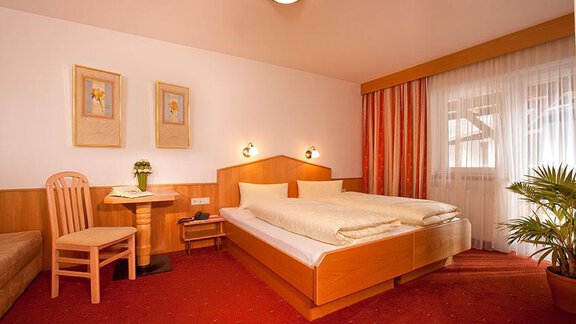 A cozy room with a double bed and wooden furniture. Large windows let in plenty of light and there is a small seating area. - Hotel Garni Ehrenreich - Sölden