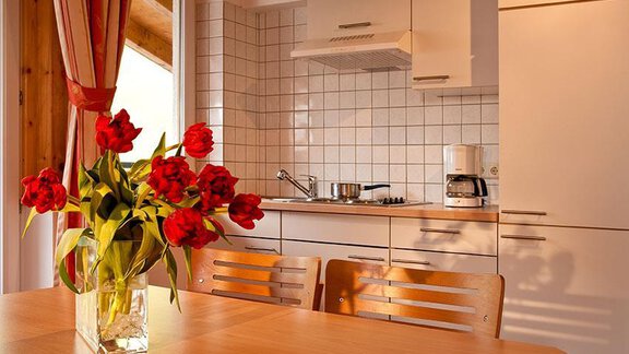 A modern kitchen with white cabinets and a light countertop. A vase with red tulips is on the table. - Hotel Garni Ehrenreich - Sölden