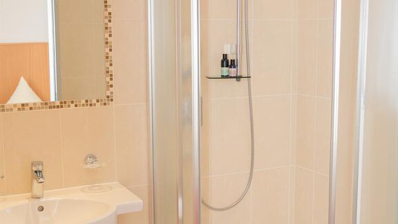 A modern bathroom with a shower cabin and a wash basin. The walls are light tiled, and there is a decorative mirror frame. - Hotel Garni Ehrenreich - Sölden
