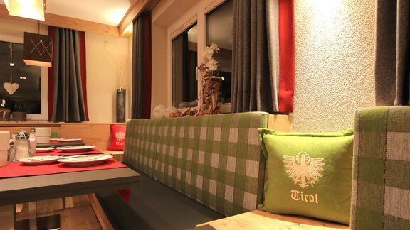 A cozy restaurant with a modern decor. The bench is green checkered and decorated with cushions printed with "Tirol." - Hotelappart Peter - Sölden | © Falkner Georg