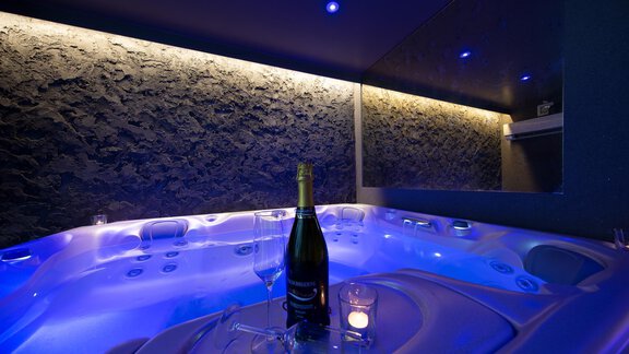 A luxurious hot tub with soft blue light. Next to the hot tub is a bottle of champagne and a glass. - Hotelappart Peter - Sölden