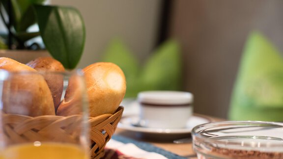 A set table with fresh rolls in a basket and a glass of orange juice. Behind it, cups and a bowl with a creamy dish can be seen. - Hotelappart Peter - Sölden | © Falkner Georg