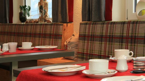 An inviting dining area with checkered benches and tables set with red tablecloths. Various plates and cups are ready for the guests. - Hotelappart Peter - Sölden | © Falkner Georg