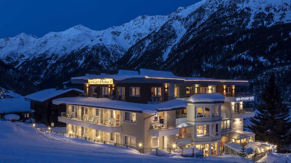A cozy hotel in the mountains, surrounded by snow-covered peaks. The facade of the building is softly illuminated and exudes an inviting atmosphere. - Hotelappart Peter - Sölden