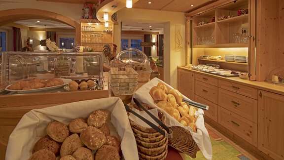An inviting breakfast area with various rolls and pastries in baskets. Bright wooden shelves and a warm atmosphere create a cozy ambiance. - Hotelappart Peter - Sölden