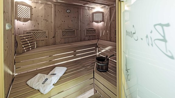 A bright wooden sauna room with benches and a wooden bowl. On one bench lies a white towel. - Hotelappart Peter - Sölden
