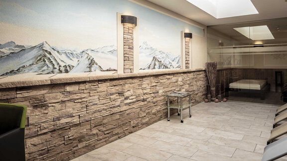 A bright room with a stone wall design and a large mural of mountains. It features modern furniture and plenty of natural light. - Hotelappart Peter - Sölden