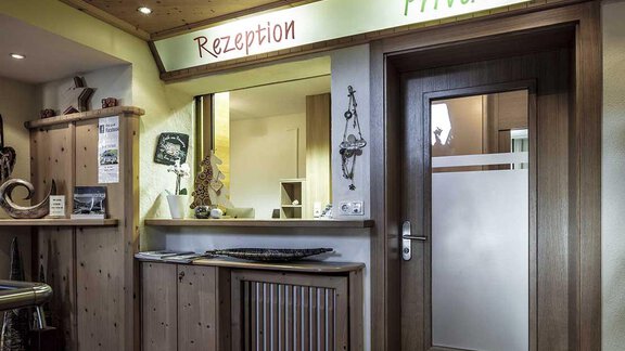 A reception area with wooden shelves and a door. The word "Reception" is written in red on the wall and "Private" in green. - Hotelappart Peter - Sölden