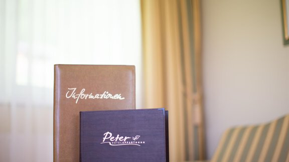 Two menu or information folders are lying on a table. The folders have different colors and inscriptions. - Hotelappart Peter - Sölden