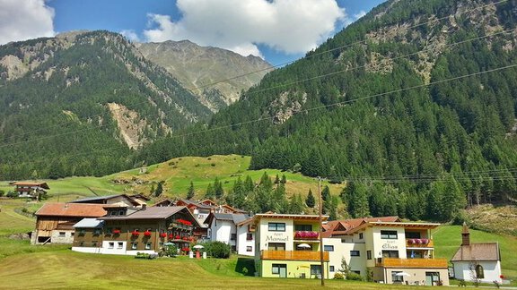 A picturesque mountain landscape with green meadows and traditional houses. In the background, high mountains and a blue sky can be seen. - Landhaus Fiegl Hubert - Sölden