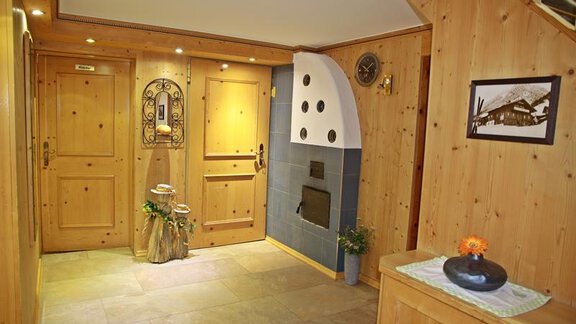 A cozy hallway with wood paneling and a classic front door. On the right side is a beautiful fireplace and a table with a coffee cup. - Landhaus Fiegl Hubert - Sölden