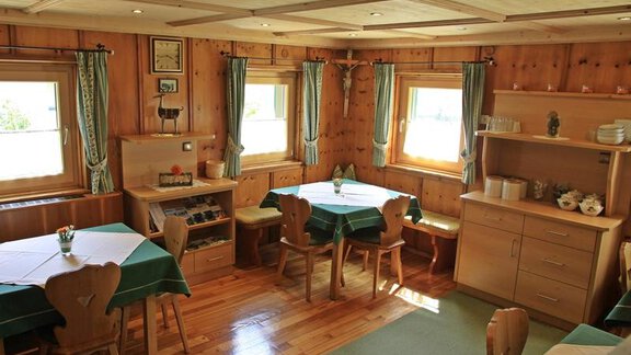 A cozy room with wooden paneling and large windows. Tables with green tablecloths and wooden chairs invite you to linger. - Landhaus Fiegl Hubert - Sölden
