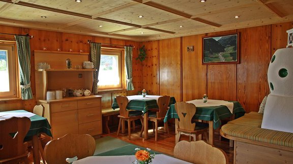 A cozy dining room with wood paneling and tables covered with green tablecloths. Light streams through the windows, creating an inviting atmosphere. - Landhaus Fiegl Hubert - Sölden
