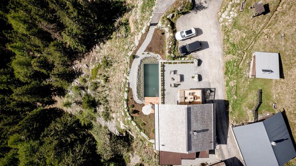 A view of an idyllic mountain cabin with a swimming pool and several vehicles. Surrounded by green forests, the area offers tranquility and nature. - LENI MOUNTAIN CHALET - Sölden