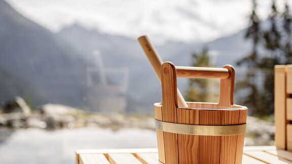 A wooden barrel stands on a wooden terrace with a view of the mountains. The scene is bright and inviting, under a cloudy sky. - LENI MOUNTAIN CHALET - Sölden