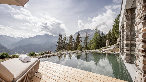 A stylish pool on a wooden terrace overlooking majestic mountains and forests. The clouds reflect in the clear water, creating a relaxing atmosphere. - LENI MOUNTAIN CHALET - Sölden