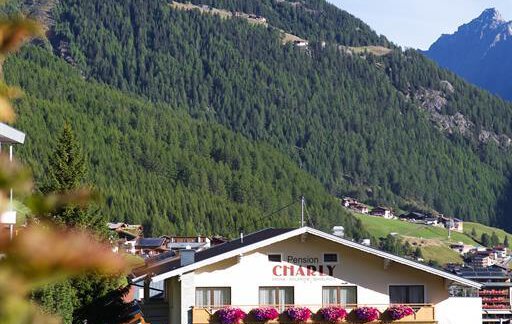 An idyllic mountain village with a charming hotel and blooming balcony flowers. Majestic mountains rise in the background under a clear blue sky. - Pension Charly - Sölden