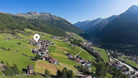 A picturesque alpine landscape with a small village in a green meadow. In the background, majestic mountains rise under a clear blue sky. - Pension Charly - Sölden