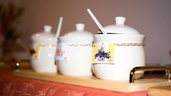 Three white sugar bowls are on a wooden board. Each bowl has a spoon and a label with a flavor. - Pension Charly - Sölden