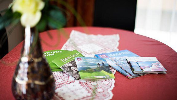 A round table with a beautiful tablecloth and a vase containing a rose. Various brochures and magazines are laid out on the table. - Pension Charly - Sölden