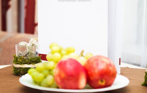 An information folder is on a table next to a plate of apples and grapes. The table is covered with a brown cloth. - Pension Charly - Sölden