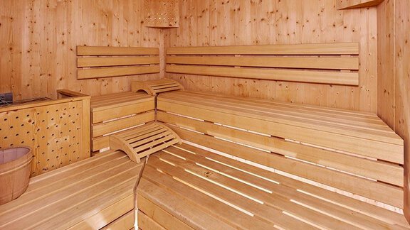 A cozy sauna room made of light wood with benches and a small container. A clock hangs on the wall, and the atmosphere is relaxing. - Pension Gritsch Ewald - Sölden